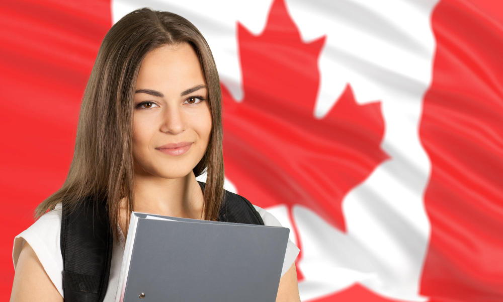 A girl holding a laptop in front of a Canadian flag.