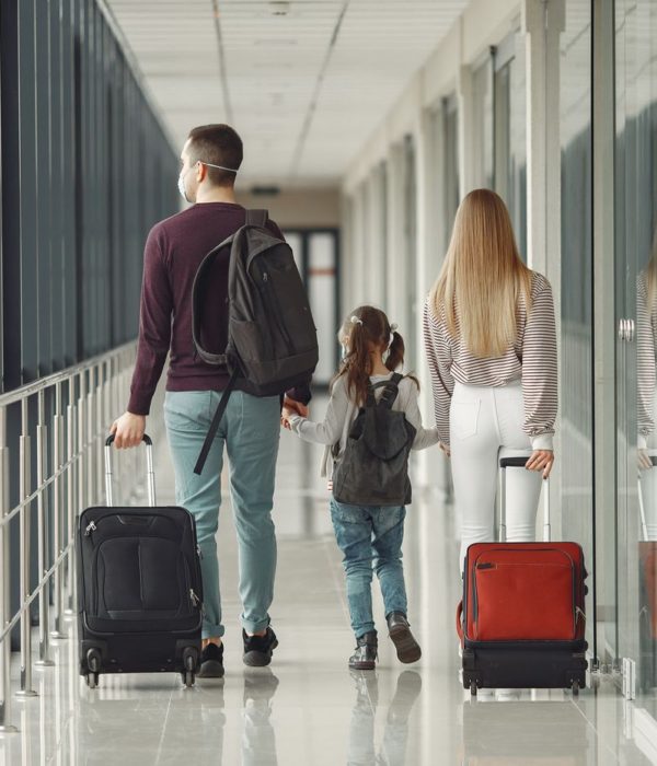 A family of three walks down an airport corridor with rolling luggage and backpacks, proudly displaying their citizenship.