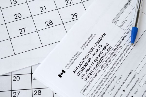 Canadian citizenship application form for adults under subsection 5(1) placed on top of a calendar, with a blue pen resting nearby and ready to help secure your future as a citizen.