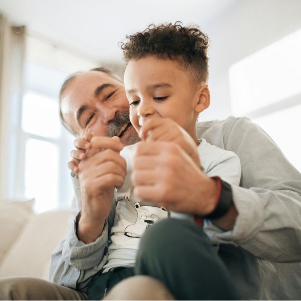 An older man and a young child, united through family sponsorship, sit on a couch, smiling and playing with hands.