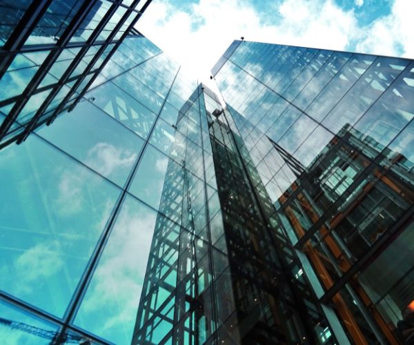 Upward view of modern glass skyscrapers, reflecting the blue sky and clouds, symbolizing the limitless potential of the Global Talent Stream.