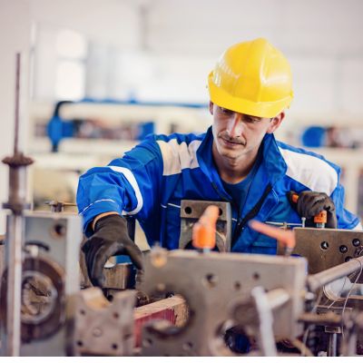 A worker in a blue uniform and yellow helmet operates machinery in an industrial setting, showcasing skills that can open doors to permanent residence through the Express Entry program.