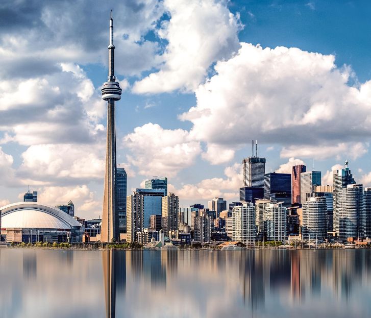 The Toronto skyline, a testament to the Canadian Dream, features the iconic CN Tower and diverse buildings reflected in Lake Ontario under a partly cloudy sky, blending reality with aspiration.